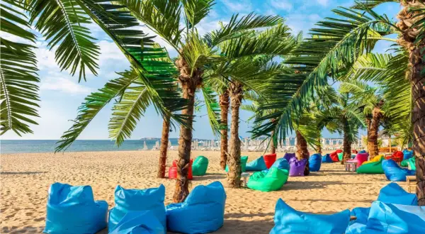 Kolorowe pufy i palmy na plaży w Bułgarii. Złote Piaski oferują mnóstwo atrakcji dla każdego.