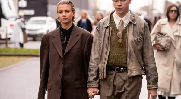Ein Paar im **Copenhagen Style** geht Händchen haltend. Sie trägt einen braunen Oversize-Blazer, er eine Lederjacke über einem Strickpullover.