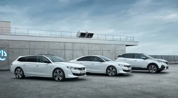Trzy białe samochody Peugeot 508: kombi, sedan i SUV, stoją przed betonowym budynkiem.