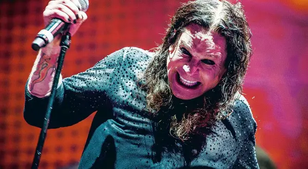 Ozzy Osbourne, wokalista Black Sabbath, z mikrofonem w dłoni, z charakterystycznym wyrazem twarzy na koncercie.