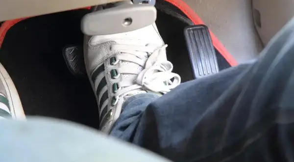 Pédale de frein enfoncée, signe d'un symptôme air dans circuit de freinage. La chaussure blanche à rayures vertes est sur la pédale.