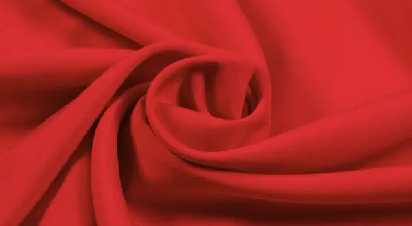 Roter Stoff, der sich zu einer Spirale drapiert. Die Textur ist glatt, was auf Lyocell oder Viskose hindeutet. Der Unterschied zwischen Lyocell und Viskose ist oft subtil.