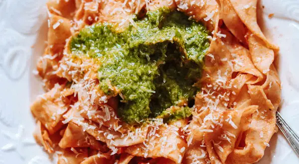 Pappardelle all'arrabbiata z zielonym pesto i parmezanem. Szerokie wstążki makaronu w sosie pomidorowym, przykryte intensywnym, zielonym pesto.