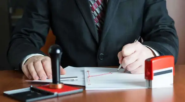 Notaio firma documenti, con timbro e inchiostro pronti per il deposito prezzo.