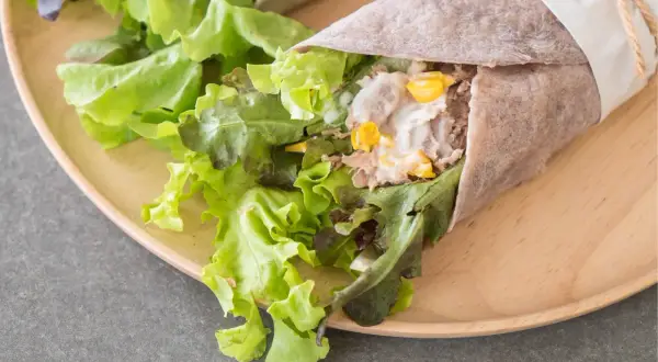 Świeża tortilla z tuńczykiem, chrupiącą sałatą i kukurydzą, zawinięta w papier i przewiązana sznurkiem.