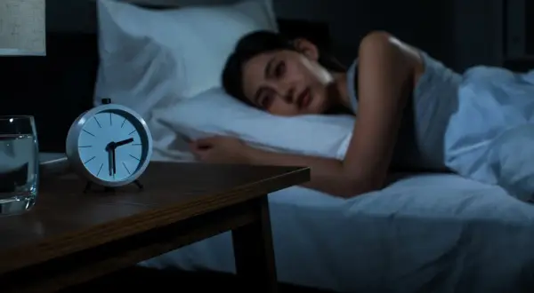 A woman lies awake in bed, staring at the clock. She's trying to figure out how to fall back asleep.