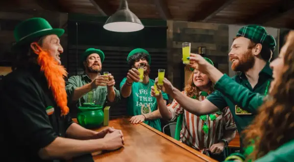 Glada människor med gröna hattar och skägg skålar med gröna drinkar vid en bardisk. Perfekt för roliga teman!
