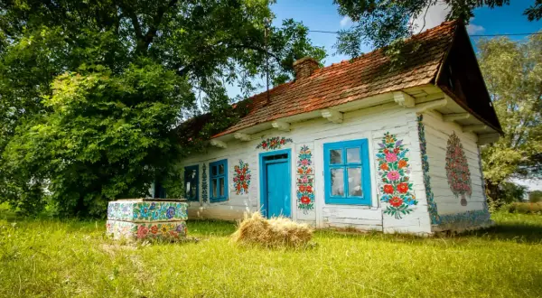 Kolorowy dom z niebieskimi oknami i drzwiami, ozdobiony ludowymi wzorami kwiatowymi. To typowy widok dla wsi Zalipie.