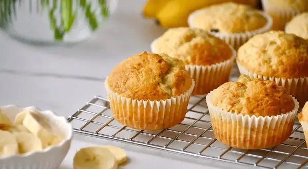 Frisch gebackene bananen muffins auf einem Gitter, daneben eine Schüssel mit Bananenscheiben.