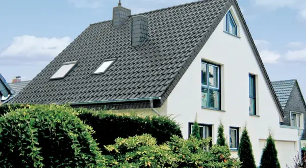 Nowoczesny dom z dachem pokrytym ciemną angobą ceramiczną. Wokół bujna zieleń.