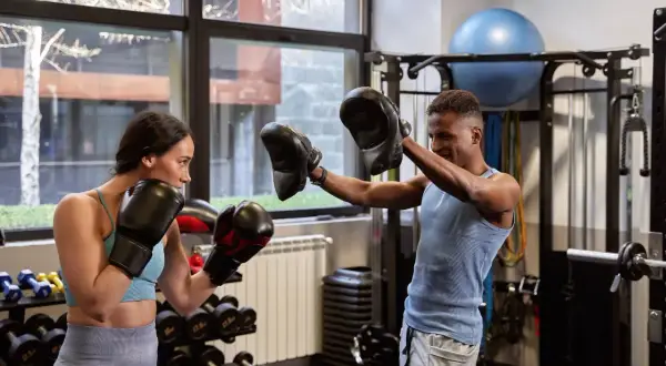 A woman and man in boxing gloves train in a gym. This is how boxers recover after a fight, by staying active and focused.