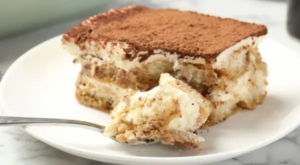 Pyszne tiramisu bez jajek na talerzu, z widocznym kawałkiem na łyżeczce.