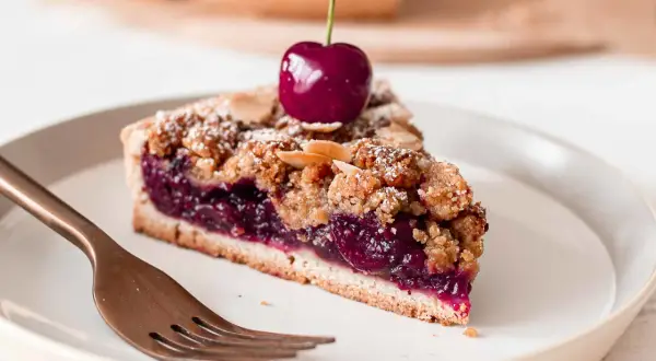 Une part de tarte aux cerises généreuse, garnie d'une cerise fraîche et saupoudrée de sucre glace et d'amandes effilées.