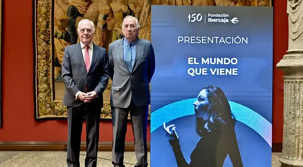 Dos hombres de traje posan ante un cartel de Fundación Ibercaja que anuncia "El mundo que viene", en un evento de martes de libros Ibercaja.