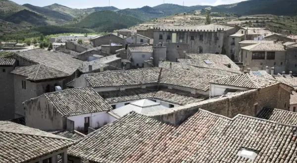 Tejado de un pueblo con colinas al fondo. Se vislumbran las torres del puente de San Valero.