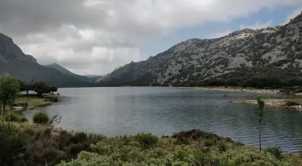 Paisaje sereno de lagos en Mallorca, rodeado de montañas rocosas y vegetación exuberante bajo un cielo nublado.
