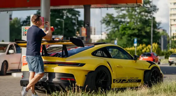 Żółty Porsche 911 GT3 RS z wielkim skrzydłem, obok którego stoi mężczyzna jedzący frytki.