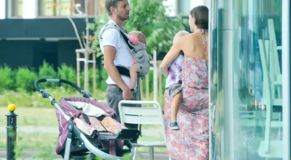 Marcin Rogacewicz z dwójką dzieci, jedno w nosidle, drugie na rękach mamy, obok wózek.