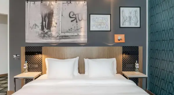 Łóżko w nowoczesnym pokoju hotelowym z białymi pościelami i ozdobami na ścianie.