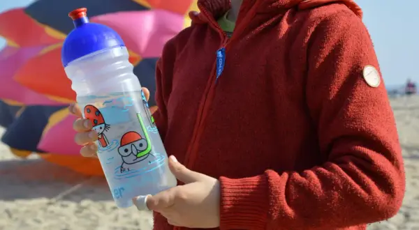 Kind hält eine isybe trinkflasche mit Tauchermotiv. Im Hintergrund bunter Drachen.