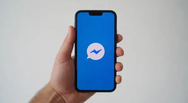 Dłoń trzyma smartfon z niebieskim ekranem i ikoną Messengera. Zastanawiasz się, dlaczego nie widzę aktywności na Messengerze?