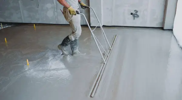 Pracownik wyrównuje świeżą wylewkę betonową. Zastanawiasz się, ile kosztuje wylewka betonowa?