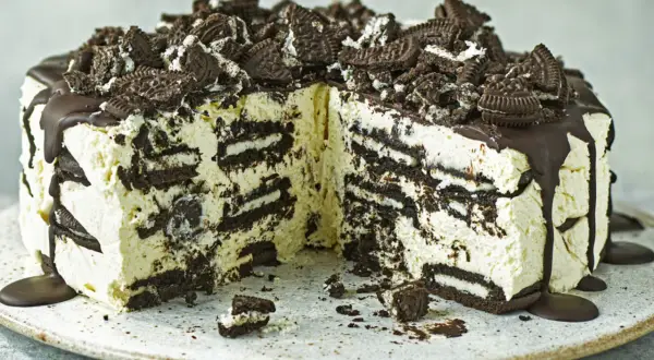 Cremige Oreo Torte mit Schokoladenguss und zerbröselten Keksen obendrauf. Ein Stück ist bereits angeschnitten.