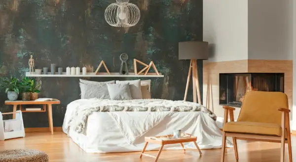 Camera da letto con un letto bianco, camino e una poltrona gialla, il tutto incorniciato da una suggestiva carta da parati effetto corten.