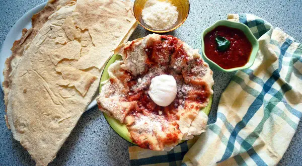 Pane carasau pronto per essere trasformato in pane frattau, con sugo di pomodoro, pecorino e un uovo in camicia.
