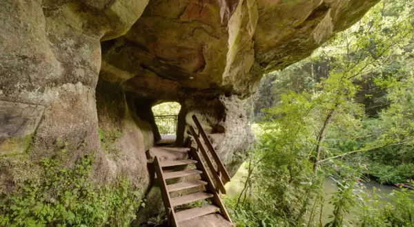 Holztreppe führt aus einer Felsgrotte auf dem schwarzachklamm wanderweg. Ein Fluss plätschert im Hintergrund.