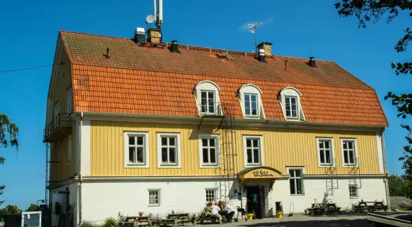 Gult hus med orange tak, "Ut Sikten" skylt. Finnhamn vandrarhem, en plats för avkoppling och naturupplevelser.