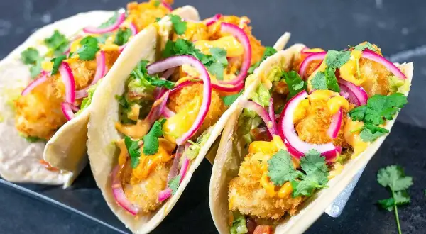 Fisktacos recept: Krispiga fiskbitar, krämig sås, rödlök och koriander i mjuka tortillabröd. En fest för smaklökarna!