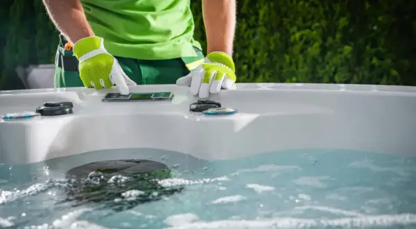 Osoba w zielonej koszulce i rękawiczkach obsługuje panel sterowania jacuzzi.