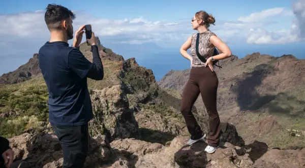 Un hombre fotografía el espectacular **barranco de Masca** mientras una mujer posa con las montañas y el mar de fondo.