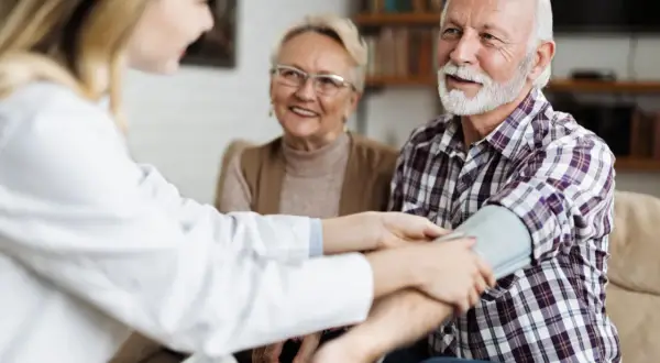 Un médecin vérifie la tension d'un homme âgé, 15/8 de tension, tandis que sa femme souriante observe.