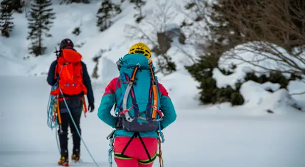 Dwóch alpinistów w zimowych strojach, z plecakami i sprzętem, przemierza ośnieżony teren. To inspiracja, co zabrać w góry zimą.