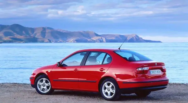 Czerwony Seat Toledo 2 na plaży, z widokiem na morze i góry w tle. Idealny na wakacyjną podróż.