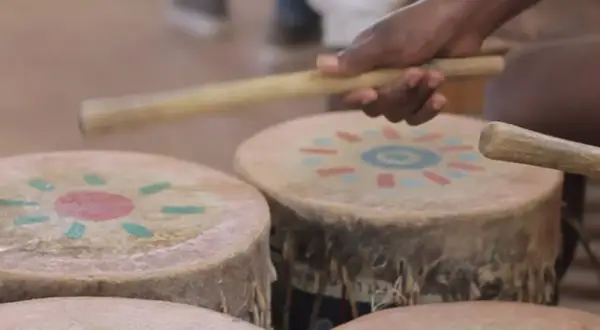 Mani che percuotono tamburi decorati con motivi solari, creando la vibrante musica africana.