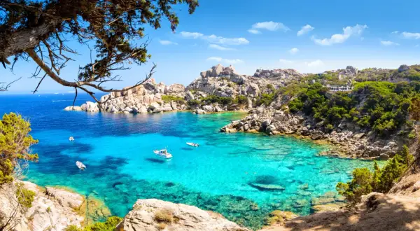 Turkusowa zatoka na Costa Smeralda, z łodziami i skalistymi brzegami porośniętymi zielenią.