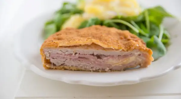 Schab po szwajcarsku, panierowany kotlet z szynką i serem, podany z sałatką.