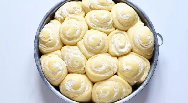 Torta di rose in teglia, soffici panini dolci con zucchero a velo, pronti per essere infornati.
