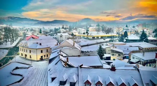 Zimowy krajobraz miasta w Czechach blisko granicy. Śnieg pokrywa dachy i ulice, a w oddali widać wzgórza.