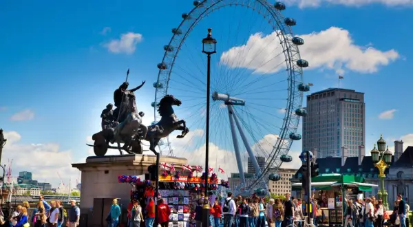 Fakta om London Eye: ett pariserhjul med gondoler, en staty av en häst och vagn, och en folkmassa på en solig dag.