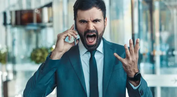 Mężczyzna w garniturze krzyczy do telefonu, pokazując, jak reagować gdy szef krzyczy.