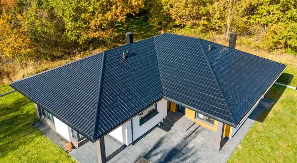 Nowoczesny dom z ciemnym, eleganckim opierzeniem dachu, otoczony jesiennym lasem.