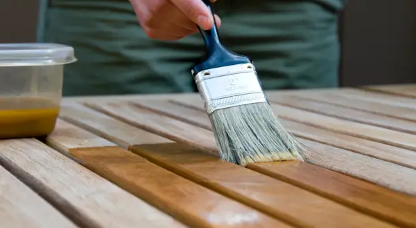Application d'une lasure acrylique ou glycéro sur des lattes de bois. La brosse dépose le produit, transformant le bois clair en une teinte plus foncée et riche.