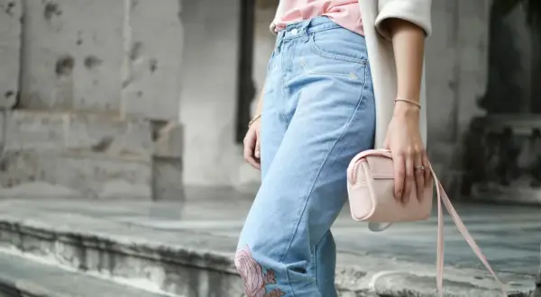 Frau in Jeans mit Blumenstickerei und rosa Tasche. Ein Symbol für die Probleme von Fast Fashion, die oft auf Kosten von Mensch und Umwelt gehen.