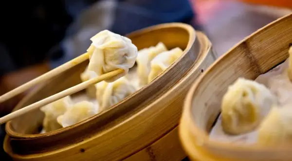 Dampfende Dumplings werden mit Stäbchen aus einem Bambuskorb gehoben. Ein köstliches Dumplings Rezept zum Nachmachen.