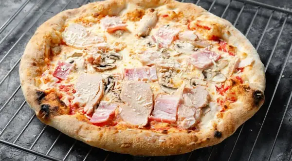 Eine knusprige Pizza mit Schinken und Pilzen auf einem Gitterrost.