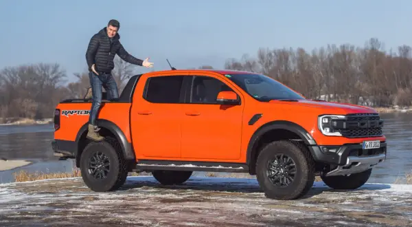 Pomarańczowy Ford Ranger Raptor z mężczyzną stojącym na pace, gotowy na przygodę.